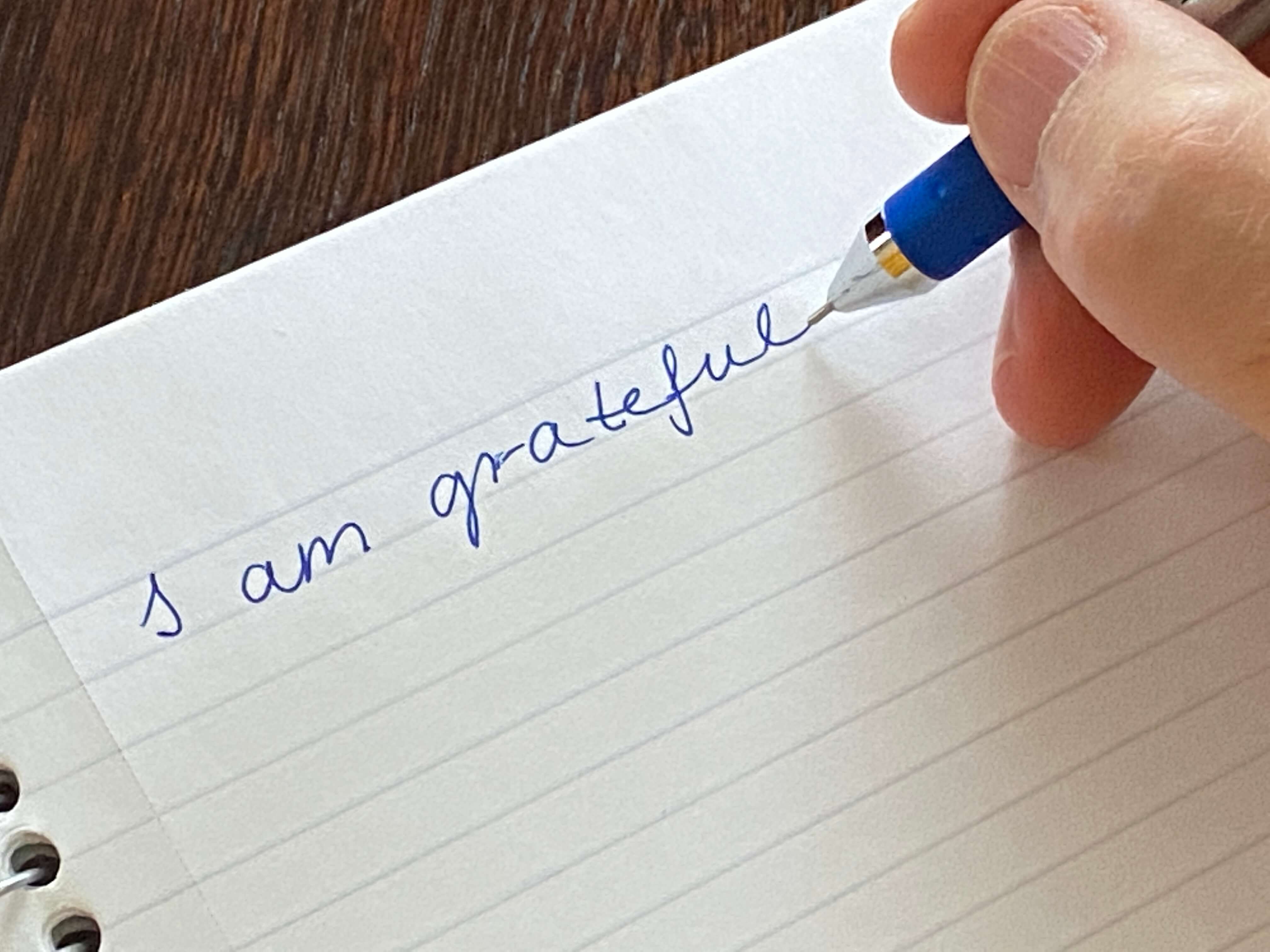 Picture of a person's hand writing I am grateful in a notebook, being grateful for a healthy lifestyle that is low carb gluten free, and grain free