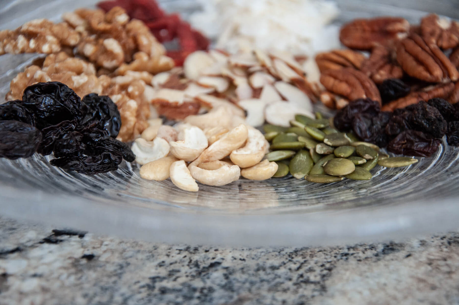 Picture of a glass plate with a mix of healthy raw nuts on it, ingredients in all flavors of JuNula just nuts granola low carb grain free gluten free granola