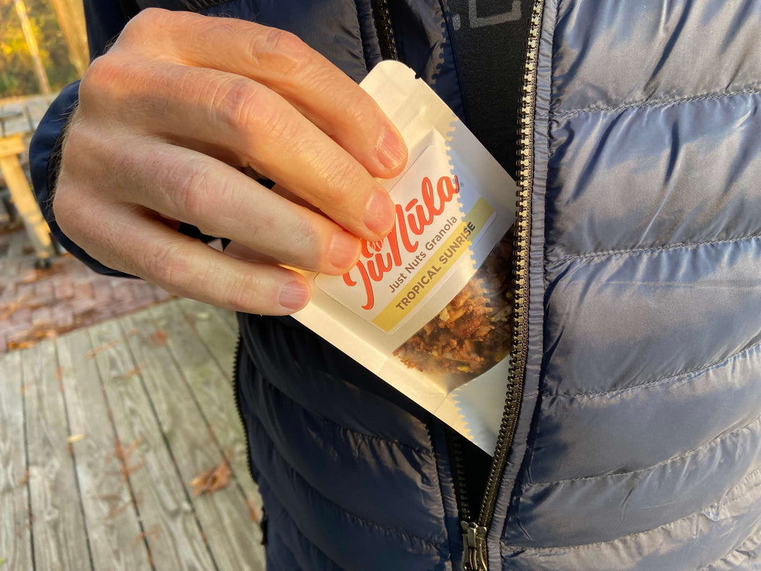 Photo of a 2oz bag of Tropical Sunrise JuNūla Just Nuts Granola being tucked into a pocket of a jacket, ready to take with you